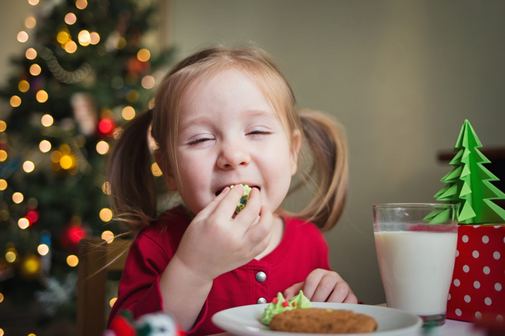 the child eats candy on the background of a Christmas tree with lights. children's xmas dinner
